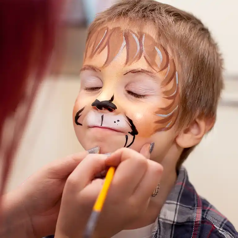 Kind bekommt beim Kinderschminken ein Löwengesicht gemalt, mit geschlossenen Augen und entspannter Miene