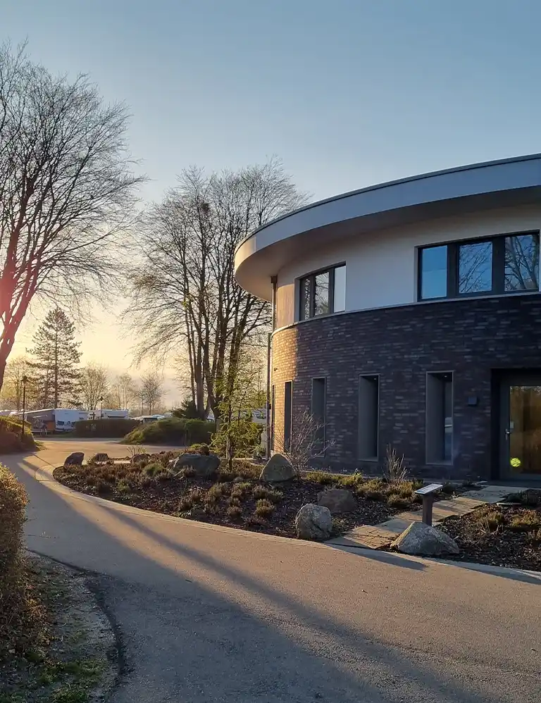 Modernes rundes Sanitärgebäude im Südsee-Camp im Abendlicht mit umliegenden Bäumen und Stellplätzen