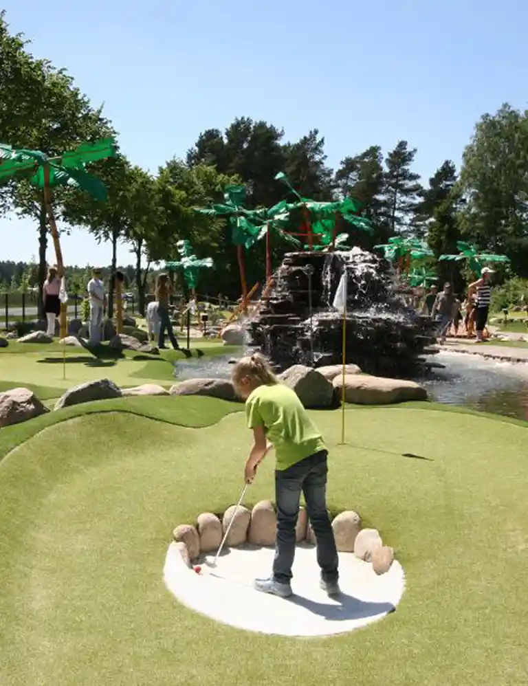 Child playing adventure mini golf at the jungle-themed course in Südsee-Camp – fun putting with waterfall and palm trees surrounded by nature