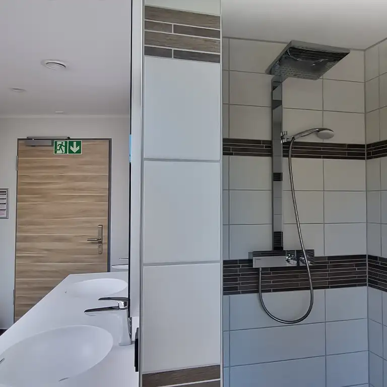 Modern private bathroom in sanitary building 4 at Südsee-Camp with rain shower, handheld shower, and double sink.