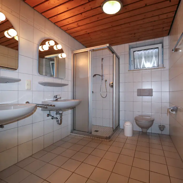 Private bathroom of the standard category at Südsee-Camp featuring a shower, toilet, two sinks, and a wooden ceiling.