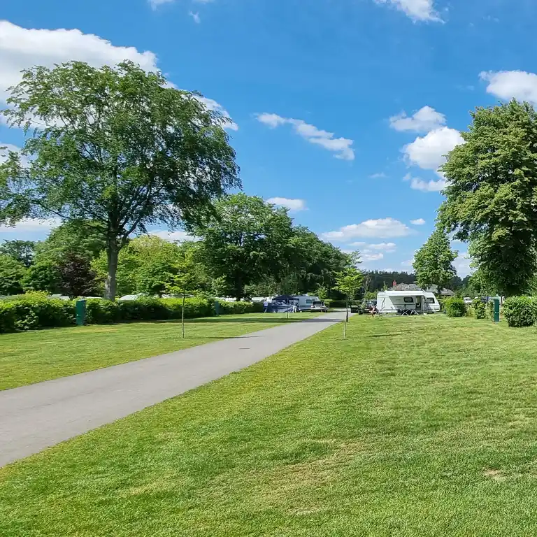 Download detailed plan Großzügiger Campingplatz mit Wohnwagen, grüner Wiese und asphaltierter Straße unter blauem Himmel