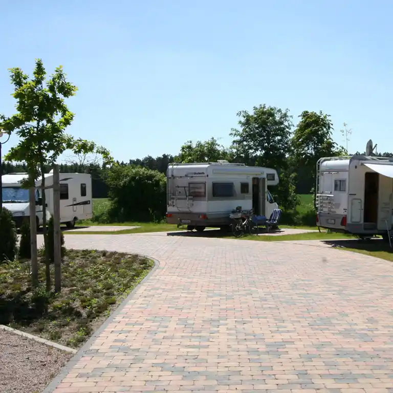 Motorhome pitch in front of Südsee-Camp with paved paths, parked motorhomes and seating areas surrounded by greenery