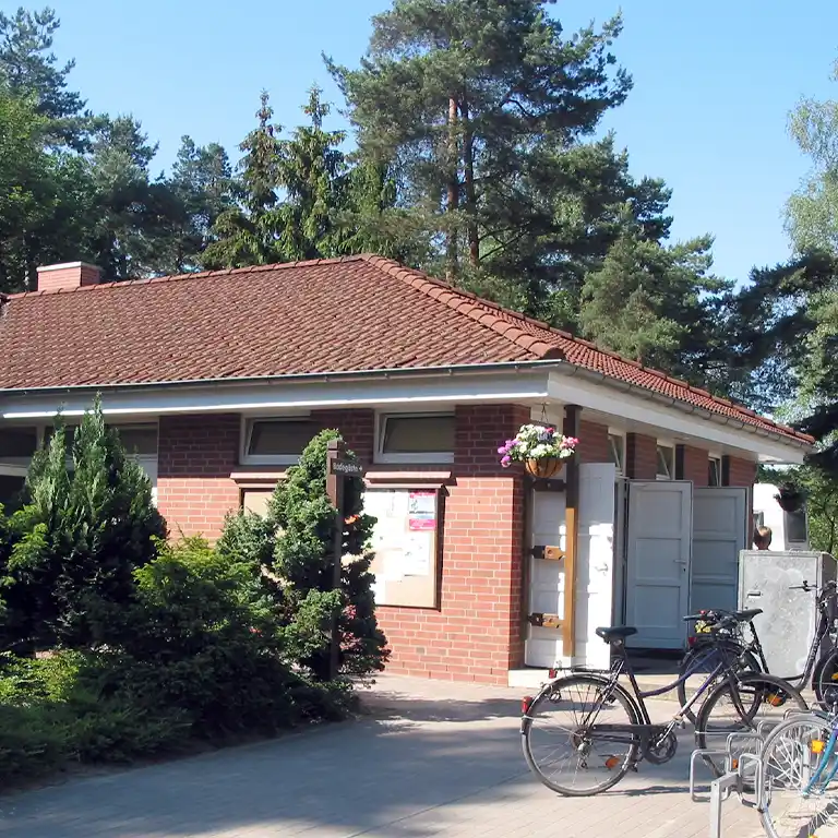 Learn more Sanitary building 1 at Südsee-Camp with red tiled roof and brick facade, bicycles in the foreground, surrounded by trees