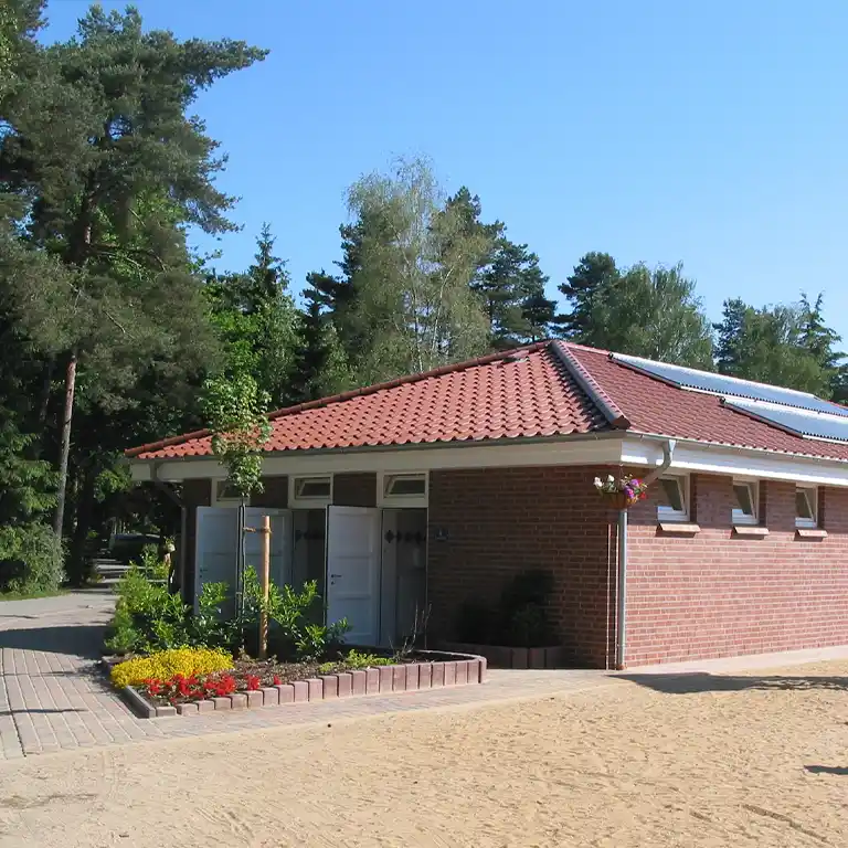 Learn more Red brick sanitary building with gable roof and solar panels, surrounded by flower beds and trees in the background.
