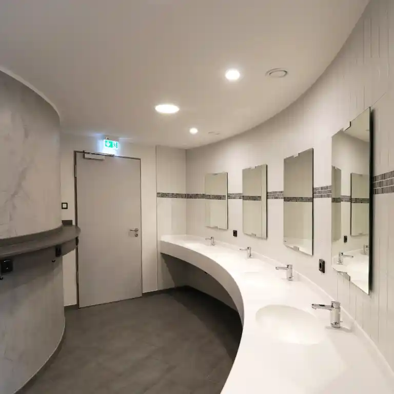 Modern sanitary building at Südsee-Camp with curved washbasin counter, multiple mirrors, and bright lighting.