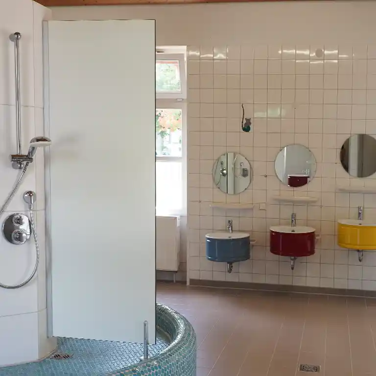 Children’s washroom in sanitary building 10 at Südsee-Camp with colorful basins in blue, red, and yellow, plus child-friendly shower – family-oriented sanitary facility at the campsite