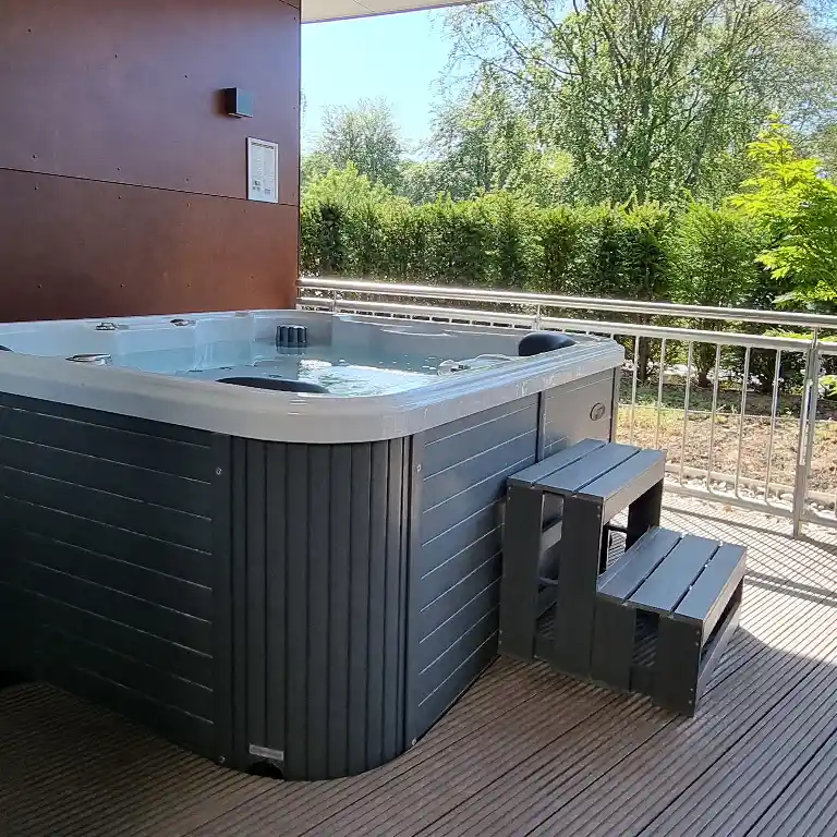 Hot tub with step access on the rooftop terrace of a private bathroom at Südsee-Camp, surrounded by greenery and privacy hedges.