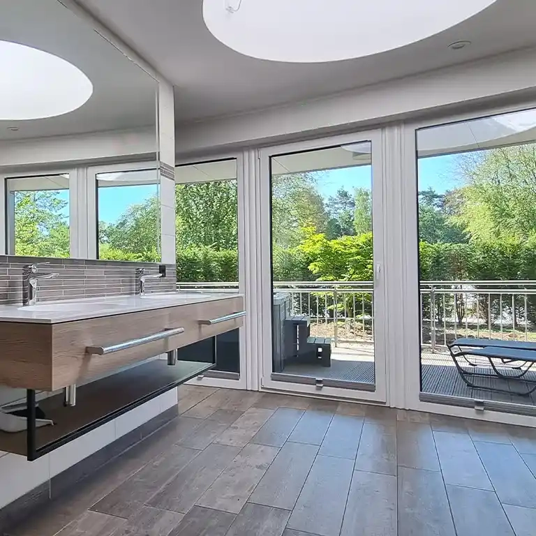 Private bathroom at Südsee-Camp featuring a modern double washbasin, large windows, and a furnished terrace with a green view.