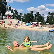 Summer break Dad happily posing with his daughter in the bathing lake, Südsee-Camp beach, lighthouse and other families in the background