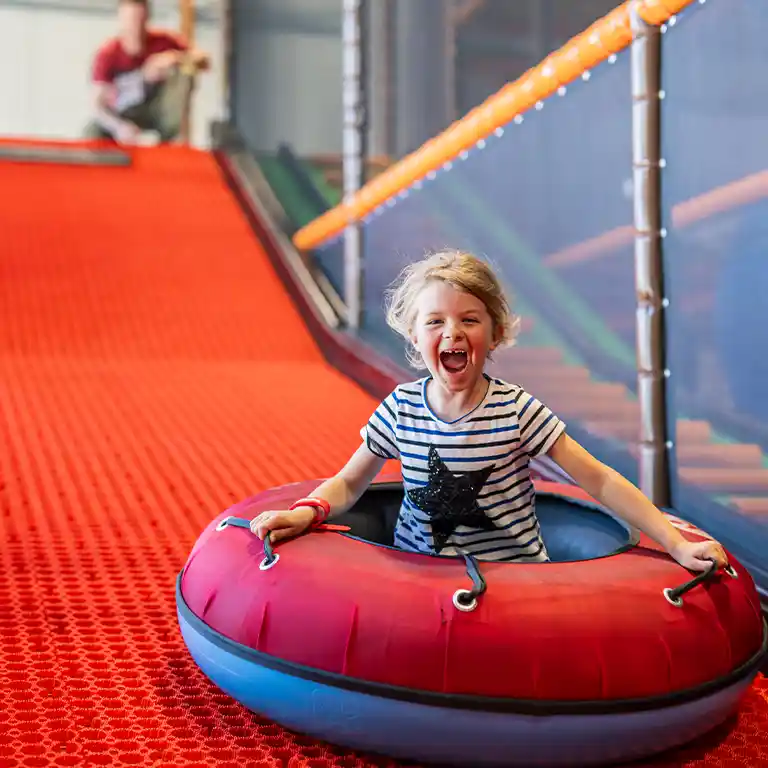 Laughing child sliding down an indoor tube slide at the ‘Piratennest’ play area in Südsee-Camp.