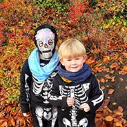 Halloween & End of Season two boys in skeleton costumes in front of autumn leaves
