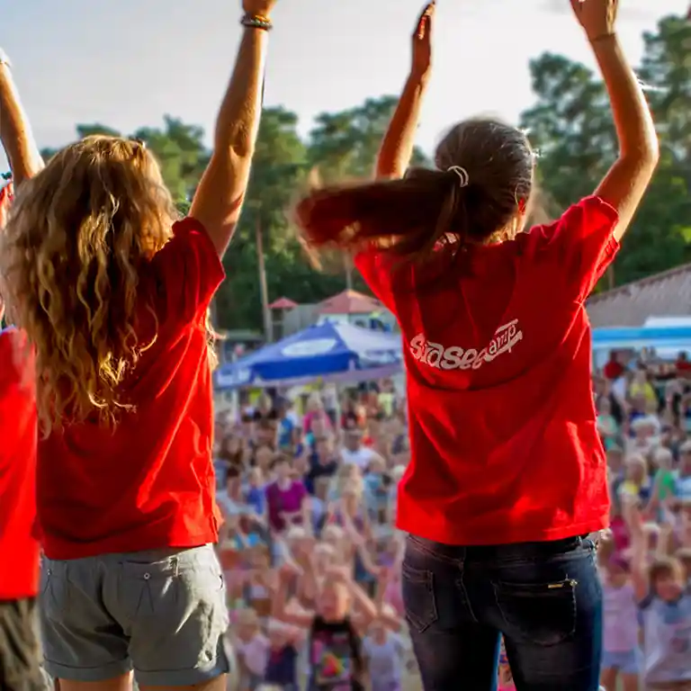 Two entertainers on stage lead the crowd with energetic movements – in the background, families enjoy a cheerful summer event.