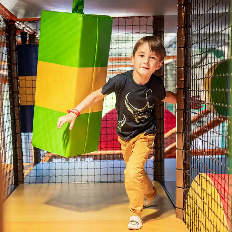 A boy runs happily through a climbing and play area at the indoor playground “Piratennest” at Südsee-Camp. Surrounded by colorful cushions and nets, he enjoys adventure and fun on a family holiday.