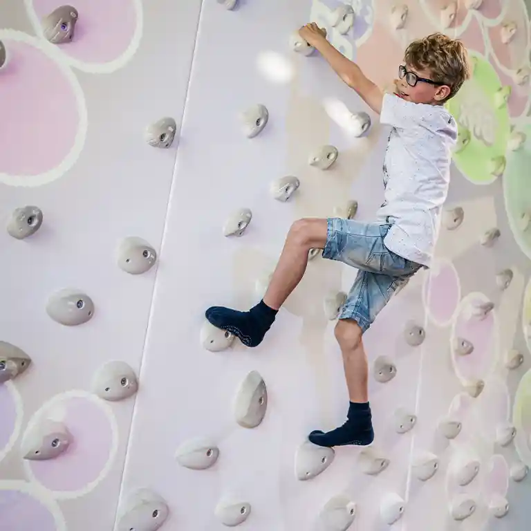 A boy climbs the virtual climbing wall at Südsee-Camp. With 3D effects and interactive holds, the wall provides sporty fun and adventure for kids on a family holiday.
