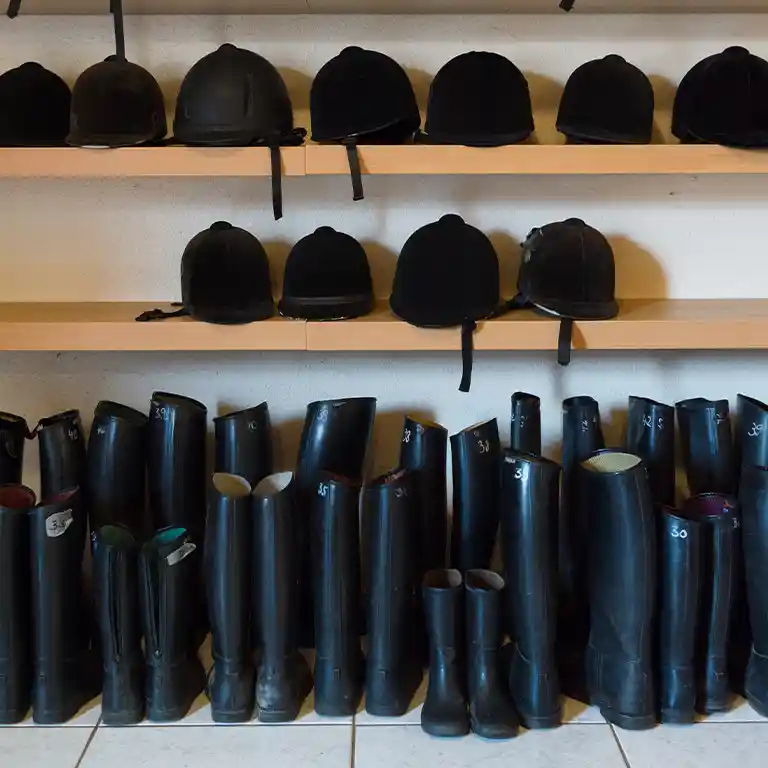 Riding equipment at Südsee-Camp: Rows of black riding helmets and rubber boots in different sizes ready for children and families – ideal for pony riding and horse holidays.