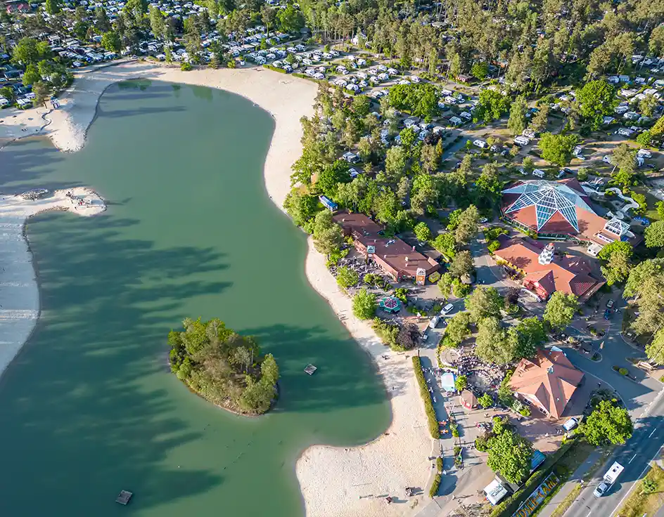 Schwimmen im Südsee-Camp: Ferienresort / Campingplatz mit Schwimmbad und Badesee Luftaufnahme des Südsee-Camps mit Badesee, Sandstrand, Insel, tropischer Badelandschaft, Restaurants und umliegendem Campingplatz im Kiefernwald.