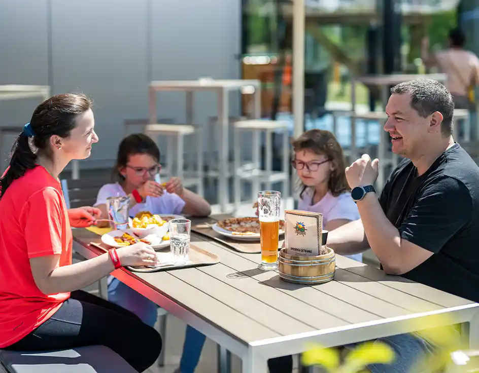 Food & drink: Restaurants, bars & snack bars at Südsee-Camp Wietzendorf Family enjoying fries and pizza at a modern outdoor table on the sunny terrace of the Piratennest at Südsee-Camp