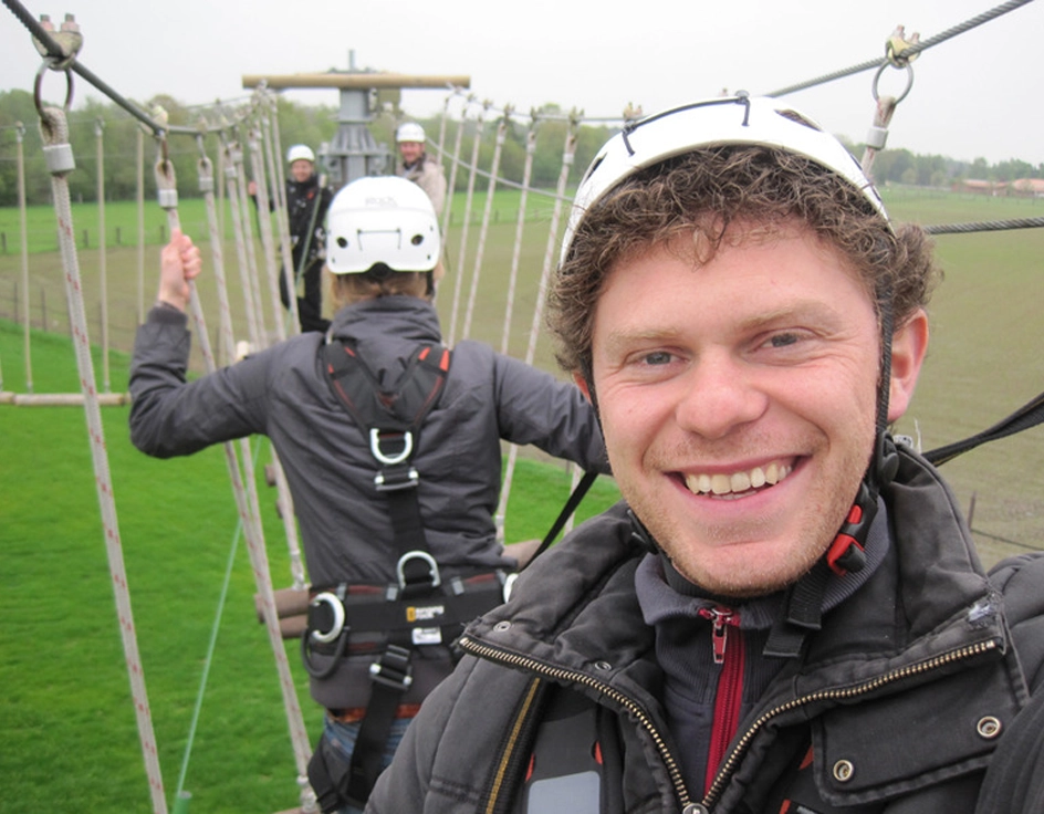 Lächelnder Mann mit Kletterausrüstung auf dem Hochseilgarten-Parcours im Südsee-Camp – Abenteuer und Nervenkitzel in luftiger Höhe.  Alt Text (English):