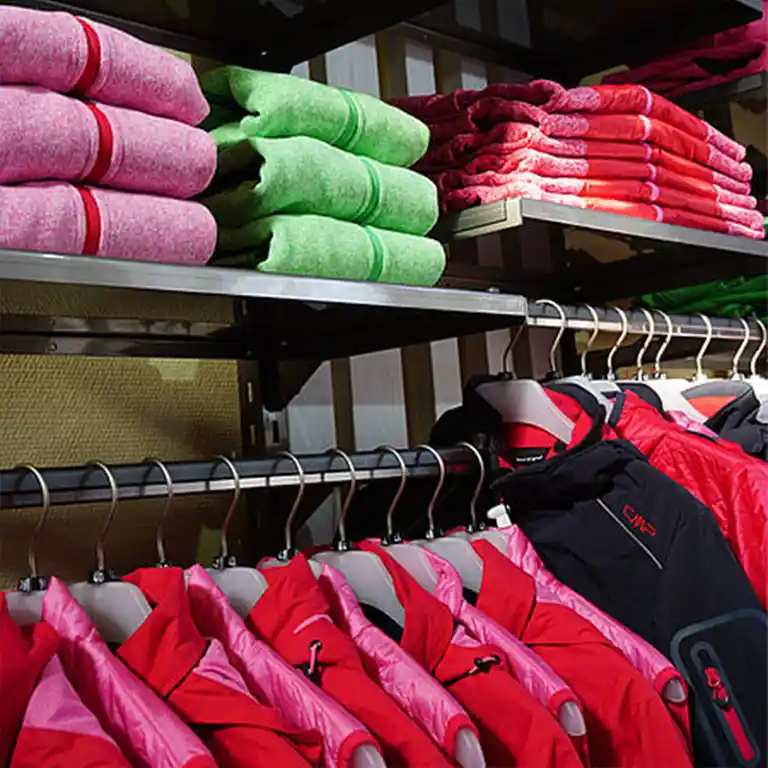 Red outdoor jackets on hangers and folded fleece jackets in pink, green, and red on the shelf at the Südsee-Trends Shop.