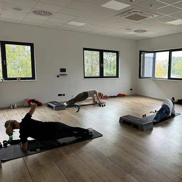 Fitness class in a bright exercise room at Südsee-Camp with three adults working out – suitable for all age groups.