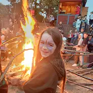Corpus Christi Girl baking bread on a stick in front of a large campfire