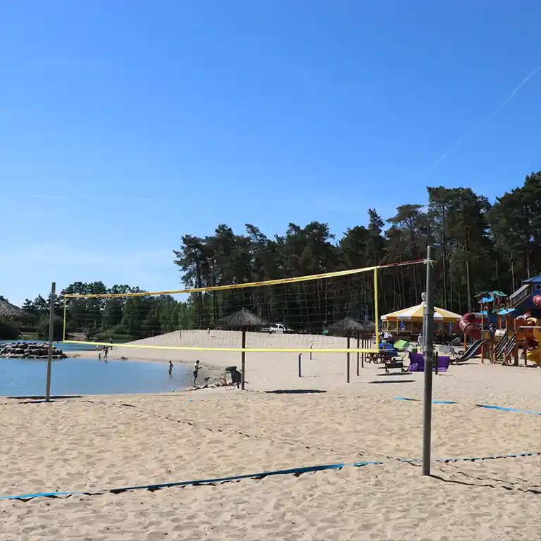 Soft sandy beach with a beach volleyball court, gently sloping lake access, and a playground connected by easy-to-navigate paths – a relaxing spot for families.