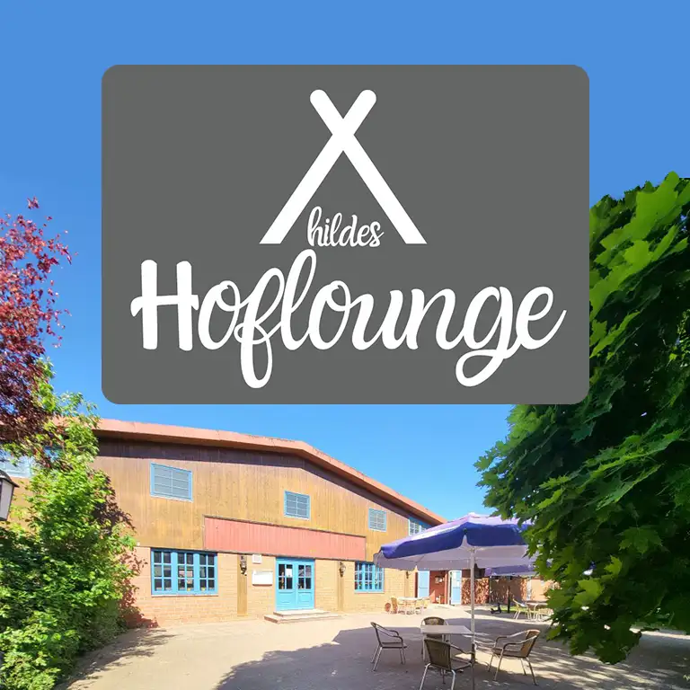 Outdoor area of Hildes Hoflounge at the riding stables of Südsee-Camp, featuring cozy seating under umbrellas in front of a rustic wooden building – perfect for relaxing after horseback riding or visiting the farm.